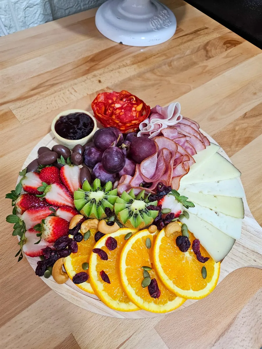 Tabla de charcutería circular con quesos, jamón, naranjas, kiwi y frutos rojos